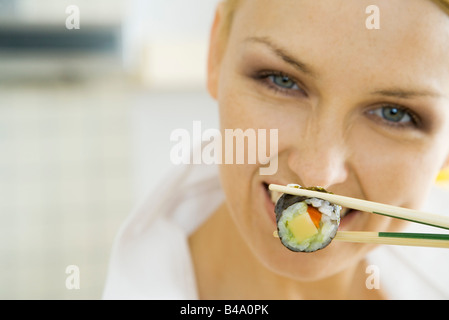 Woman holding sushi roll with chopsticks, smiling Stock Photo