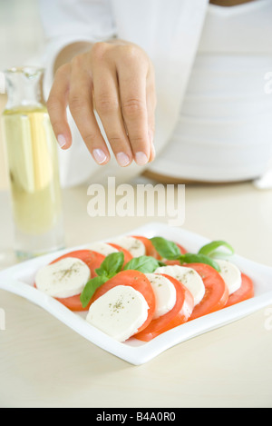 Woman preparing dish of Caprese salad, sprinkling pepper Stock Photo