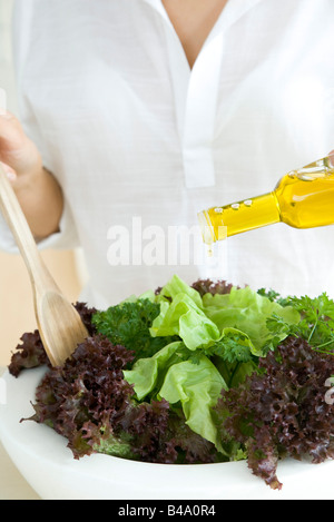 Woman preparing salad, pouring olive oil dressing Stock Photo