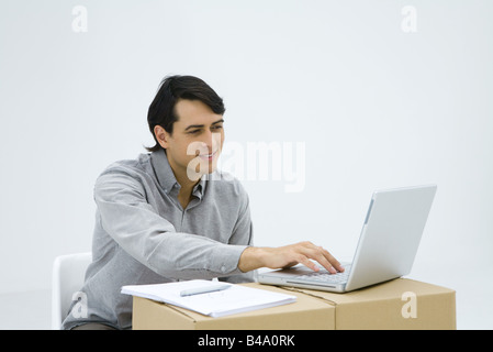 Man sitting at cardboard box desk, using laptop computer Stock Photo