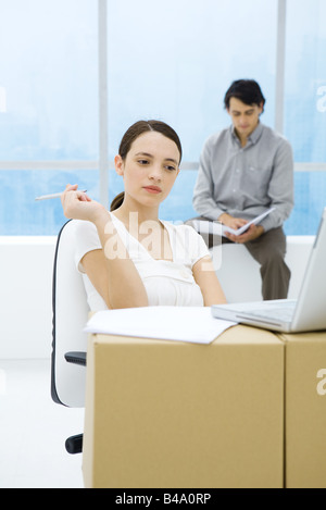 Young woman sitting at cardboard box desk, looking at laptop computer Stock Photo