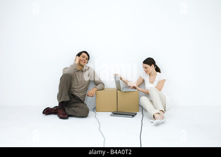 Man talking on phone, sitting on floor next to woman using laptop computer at cardboard box desk Stock Photo