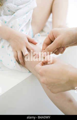 Woman putting adhesive bandage on little girl's knee, cropped view Stock Photo