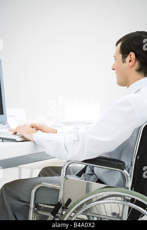 Professional man in wheelchair, typing, side view Stock Photo