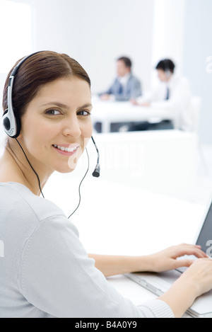 Woman wearing headset, working at desk, smiling over shoulder at camera Stock Photo