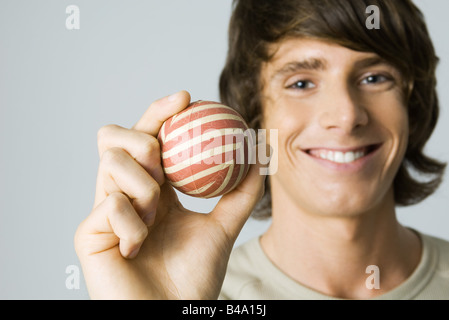 Young man holding striped ball, smiling at camera Stock Photo