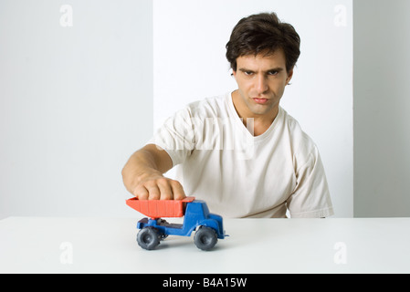 Man playing with toy dump truck, looking at camera with furrowed brow Stock Photo