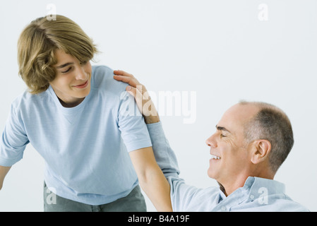 Man sitting with hand on teen son's shoulder, both smiling Stock Photo