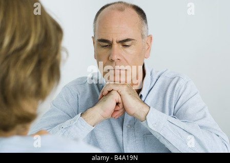 Man resting chin on clasped hands, looking down, over the shoulder view Stock Photo