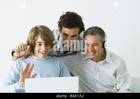 Father and two sons looking at laptop computer together, father wearing headphones Stock Photo