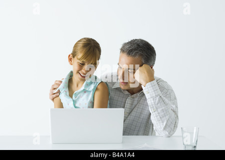 Father and daughter looking at laptop computer together, both smiling Stock Photo