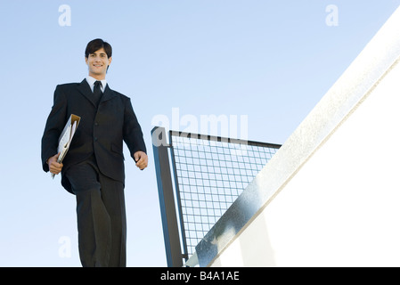 Businessman walking outdoors, carrying folder, low angle view Stock Photo