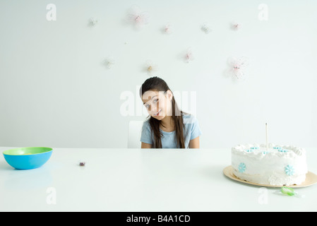 Girl sitting at table with birthday cake, smiling at camera Stock Photo