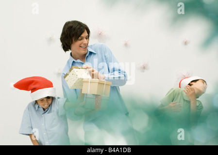 Young man with presents, playing with two boys wearing Santa hats Stock Photo