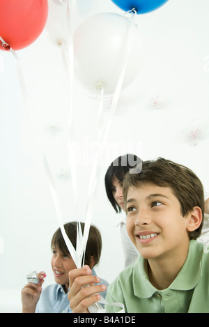 Boy holding balloons, smiling, family in background Stock Photo