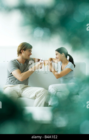 Couple sitting together on sofa, toasting with champagne Stock Photo