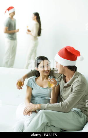 Couple at Christmas party, sitting together on sofa, champagne glasses in hands Stock Photo