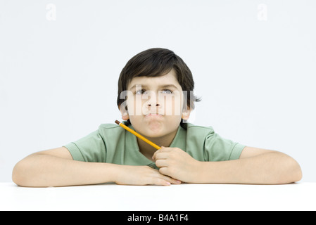 Boy holding pencil, biting lips, looking up Stock Photo