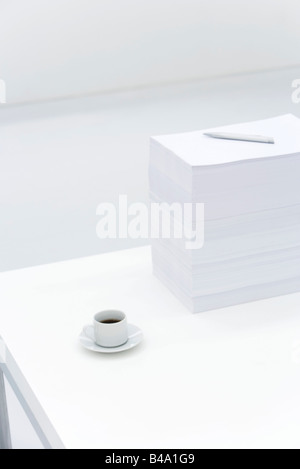 Coffee cup and large stack of documents on desk Stock Photo