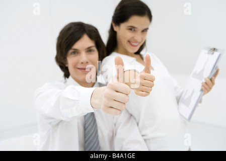 Two office workers giving thumbs up, smiling at camera Stock Photo