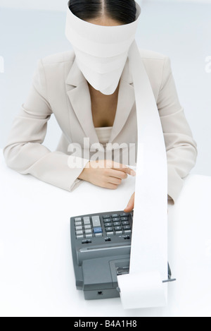 Businesswoman using adding machine, blindfolded with paper printout Stock Photo