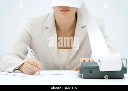 Accountant using adding machine, printout wrapped around her face like blindfold, cropped view Stock Photo