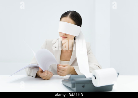 Female accountant blindfolded with paper from adding machine, holding document Stock Photo