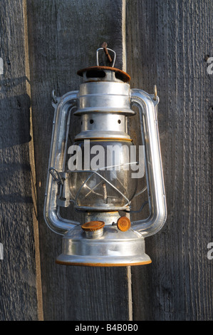 Hurricane lamp with rust hanging from a fence in evening light Stock Photo