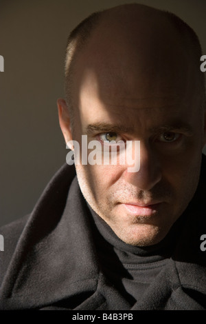 Low key portrait of a middle aged unshaven bald headed man with his collar upturned Stock Photo
