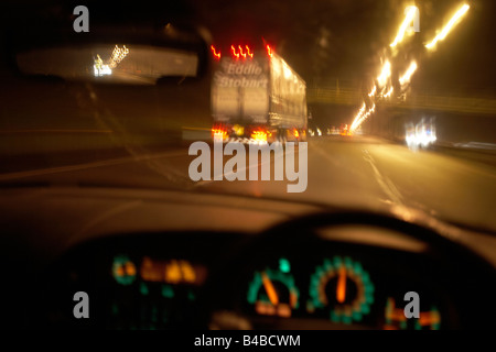 Seen through its windscreen, a car travels at high-speed along the M1 motorway behind an Eddie Stobart lorry. Stock Photo