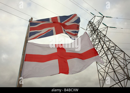 A Union Jack flag flies beneath the English Cross of St. George on a flag pole beneath an electricity pylon in a Somerset garden Stock Photo