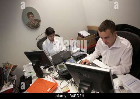 Casually-dressed accountants work in a cluttered office cubicle in an auditing company's European headquarters Stock Photo