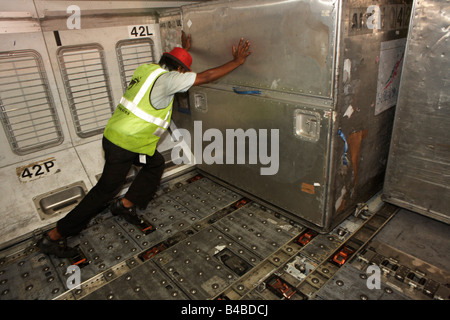 Beneath economy class flooring, a cargo handler manhandles a freight container in the hold of a Sri Lankan Airlines Airbus A340 Stock Photo