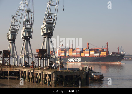 Giant cargo container ship on the River Thames eases downstream past old dock cranes at Gravesend, towards open sea at Southend