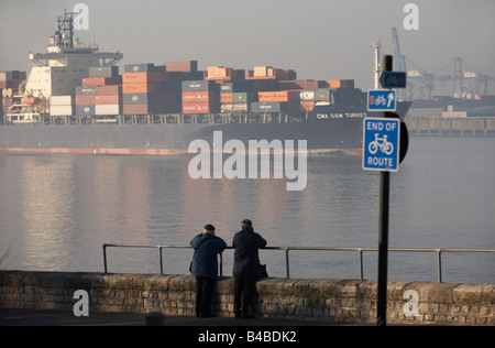 The cargo ship CMA CGM Turkey eases past two elderly ship spotters who log its details on the River Thames Stock Photo
