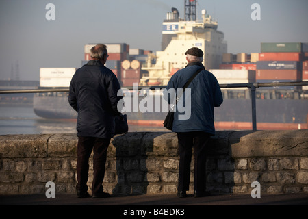 The cargo ship 'CMA CGM Turkey' eases past two elderly ship spotters who log its details on the River Thames Stock Photo