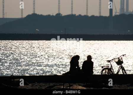 Couple two women sitting on sea shore silhouette light reflection water surface with bicycle standing talking waiting Netherland Stock Photo