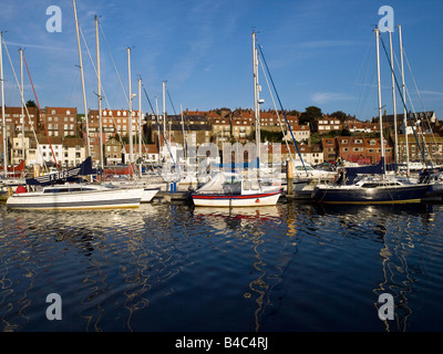 Boats and yachts lit by evening sun and reflected in the blue waters of Whitby harbour