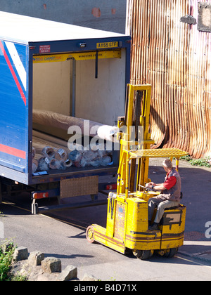 Workman operating a forklift truck, unloading carpets from a lorry Stock Photo