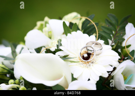 Silver white gold platinum wedding rings bands resting on white flower in bridal bouquet generic happy wedding day image Stock Photo