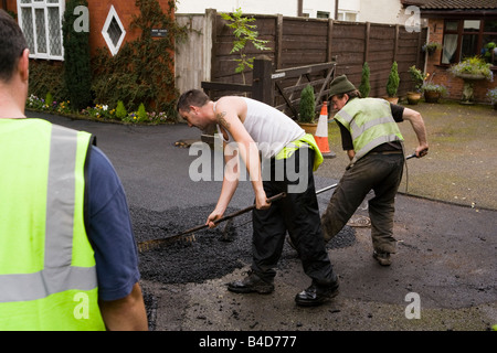 Home improvements gang of workers raking new domestic tarmac drive flat Stock Photo