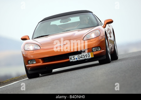 Corvette C6, rust-red model year 2008, orange -metallic, driving, diagonal from the front, frontal view, country road, closed to Stock Photo