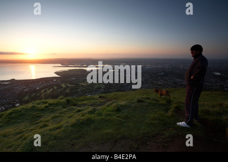 man with his dog standing admiring the view from top of Cave Hill overlooking Belfast belfast northern ireland uk Stock Photo