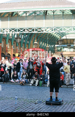 Street performer plays to a large crowd of tourists assembled outside Covent Garden, a popular sightseeing location in London UK Stock Photo