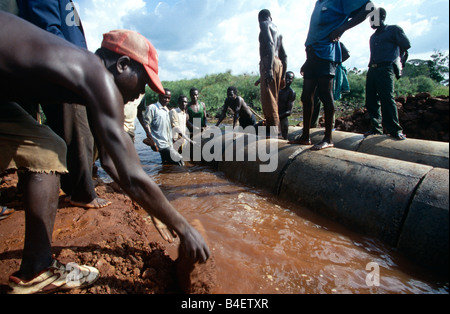 Team of workers connecting industrial pipes in rural waterway, Uganda, Africa Stock Photo