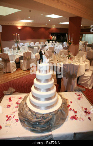 Luxury white multi tiered wedding cake with dancing bride and groom statues on top in empty wedding reception breakfast room Stock Photo