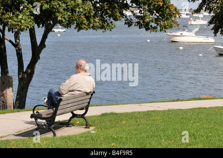 One caucasian white middle age man sitting alone on park bench by waterfront in white jacket Stock Photo