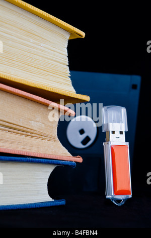 Three books and floppy disk loom menacingly over a red usb key standing upright; old media wants revenge on new digital media Stock Photo
