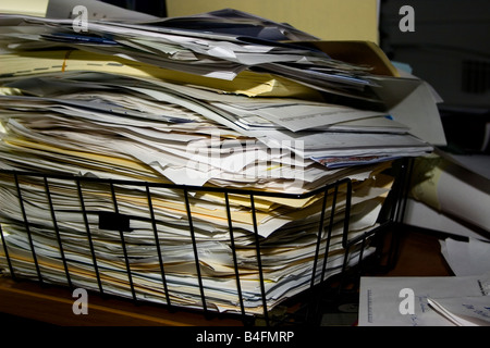 A pile of papers and file folders stacked to overflowing in a black wire basket. Stock Photo