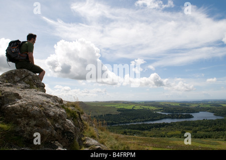 A Hiker on top of Leather Tor on Dartmoor looking out over Burrator Reservoir Stock Photo
